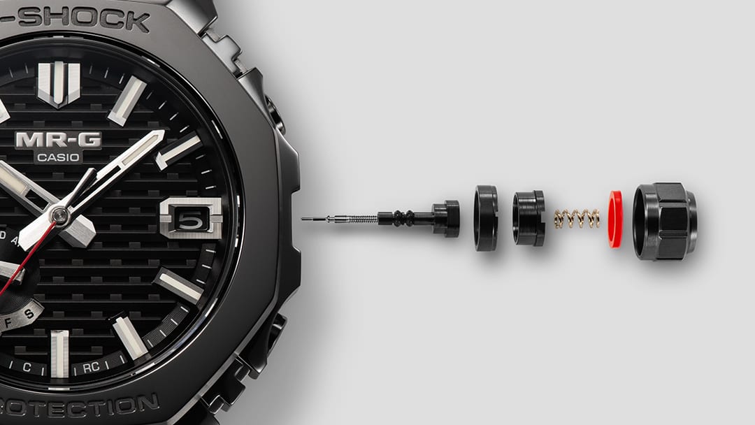 Close-up of the MRG-B2100B bezel, with the crown disassembled into its individual parts next to it.