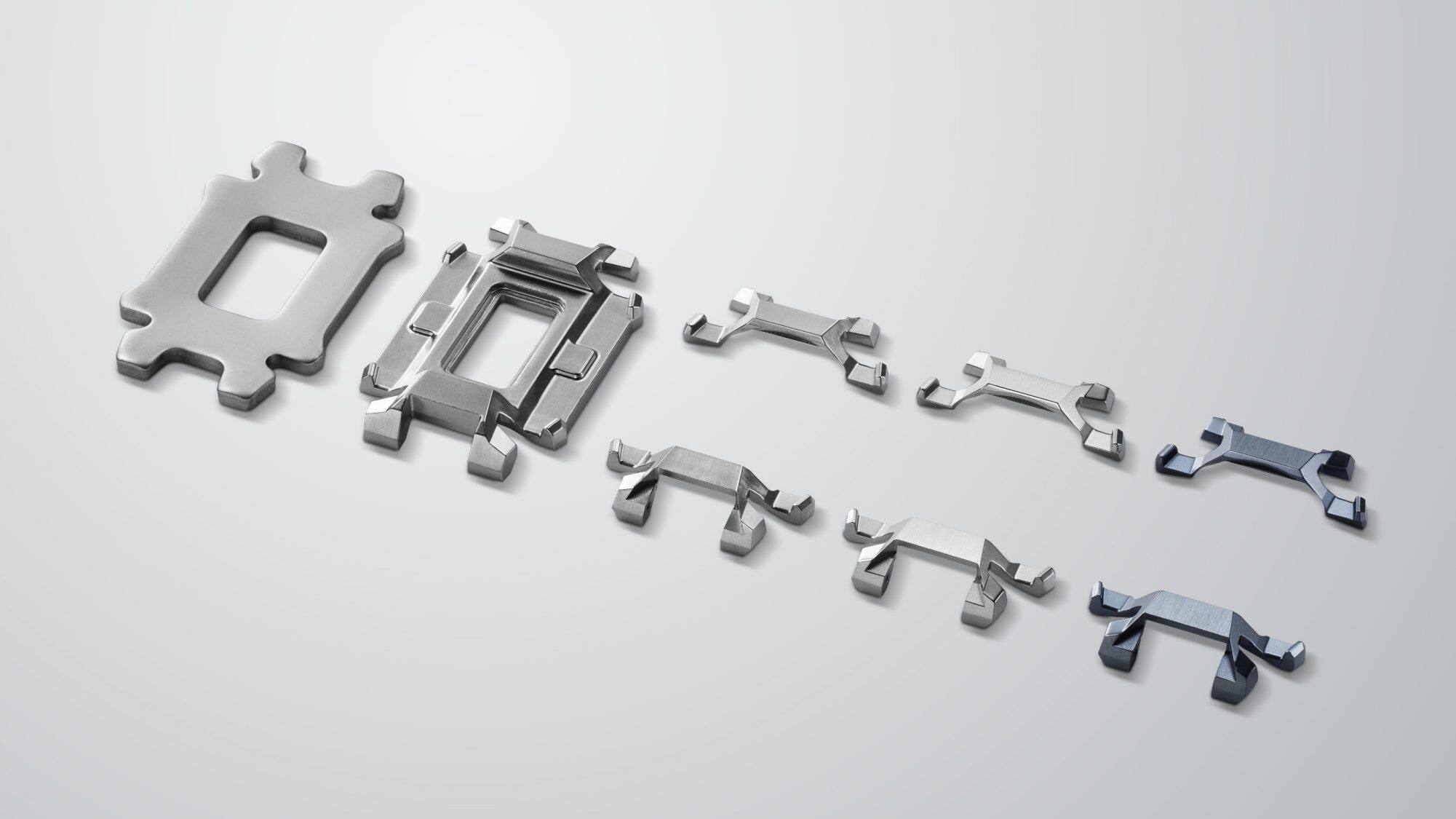 Several metal parts in various shades of silver lie on a light-coloured background