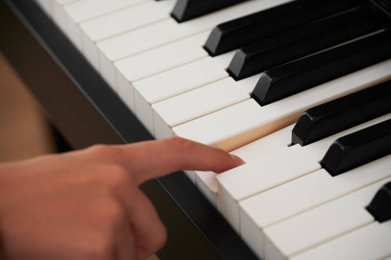 Close-up of the piano keys. A hand strikes a key with the index finger.