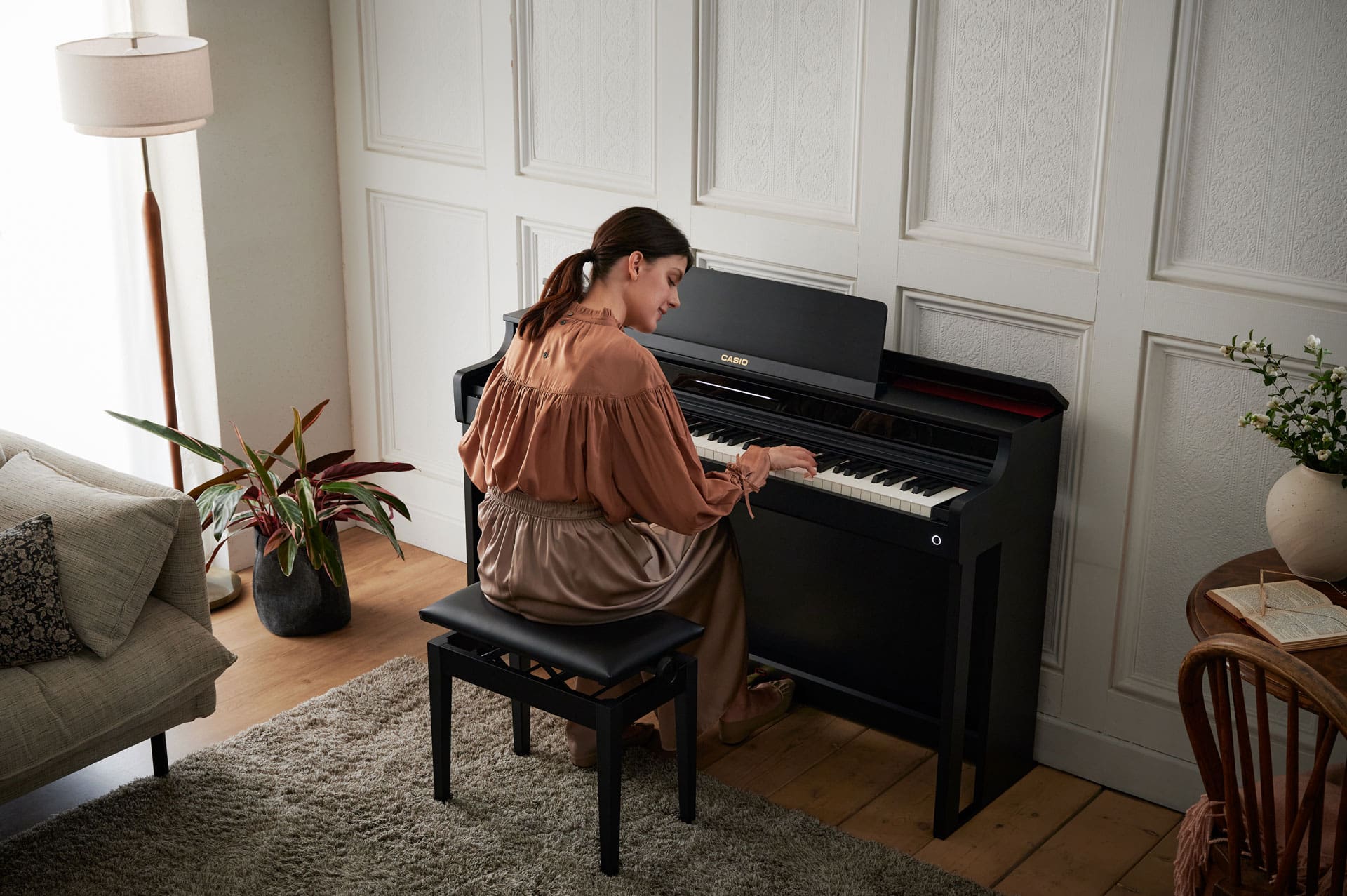 A woman sits at the black Casio AP-550BK in a comfortably furnished room and plays the piano