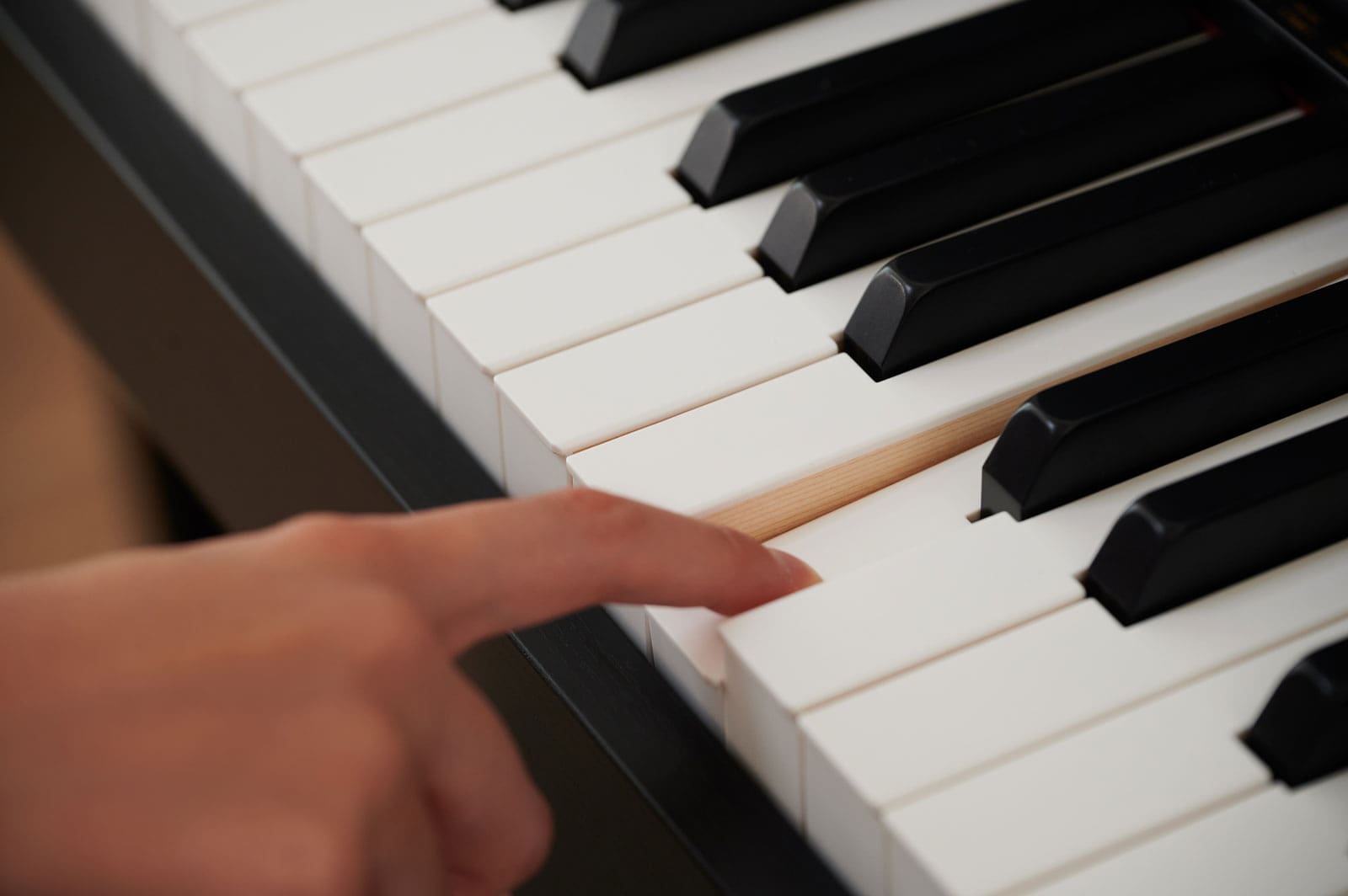 Close-up of the piano keys, one hand strikes a key with the index finger