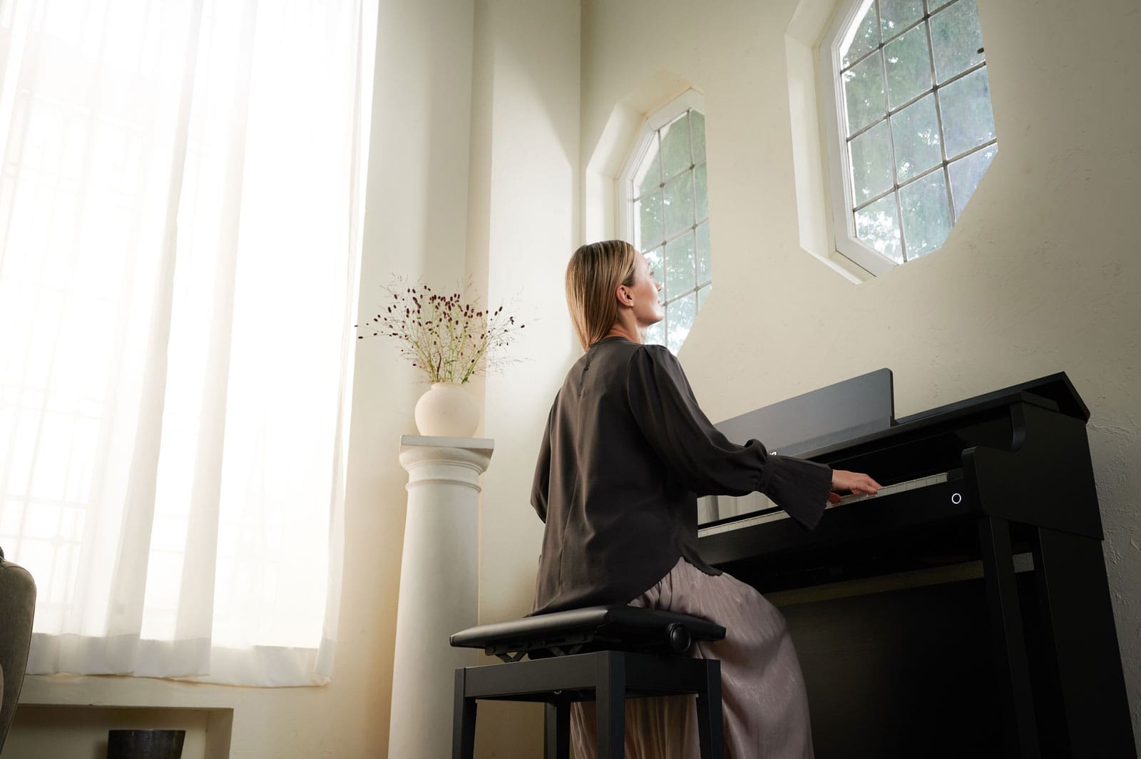 A woman sits in a brightly lit room at the black CASIO AP-750 digital piano and plays the piano.