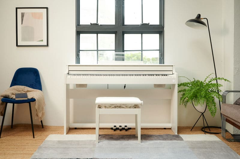 A white AP-S450 digital piano is placed in a bright living room in front of a window