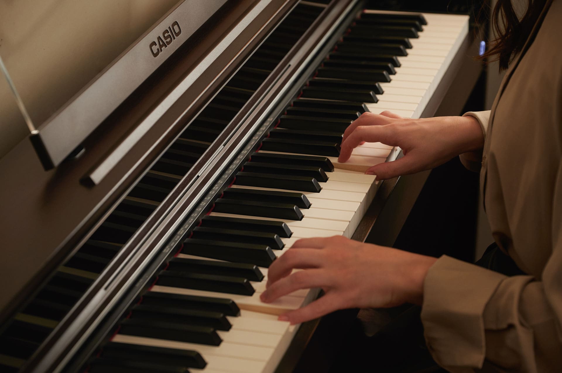 Close-up of the keyboard of a brown Celviano AP-S450 digital piano, while two hands play the piano
