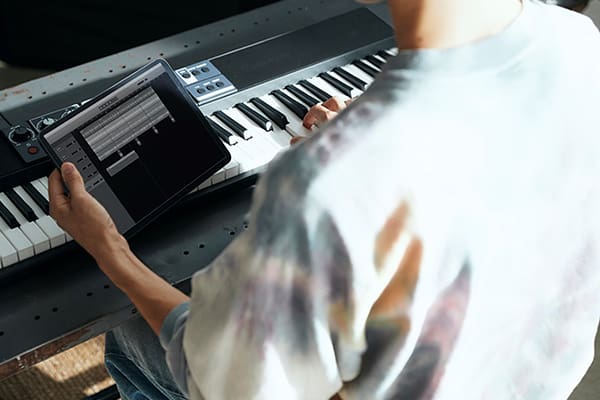 Looking over the shoulder of a person sitting at a Casiotone CT-S500 playing the piano while simultaneously looking at their tablet