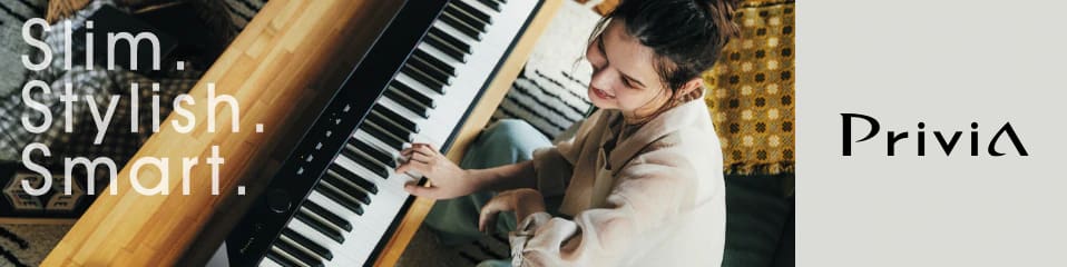 Top view of a young woman sitting at a living room table playing a black Privia PX-S1100BK digital piano. The words ‘Slim. Stylish. Smart’ are shown on the left side of the image, and ‘Privia’ is shown on the right side of the image in black letters on a light grey background. The image links to the Privia Brand Site on music.casio.com/intl.