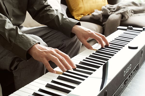 Close-up of the keyboard of the black Privia PX-S6000 digital piano and man's hands playing the piano