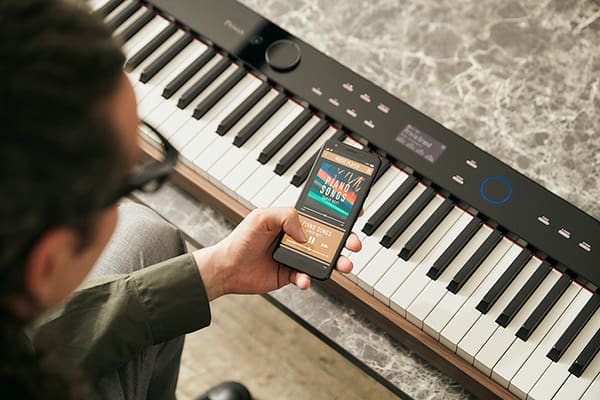 Someone is operating the music player on their smartphone directly above the keyboard of a PX-S6000 digital piano