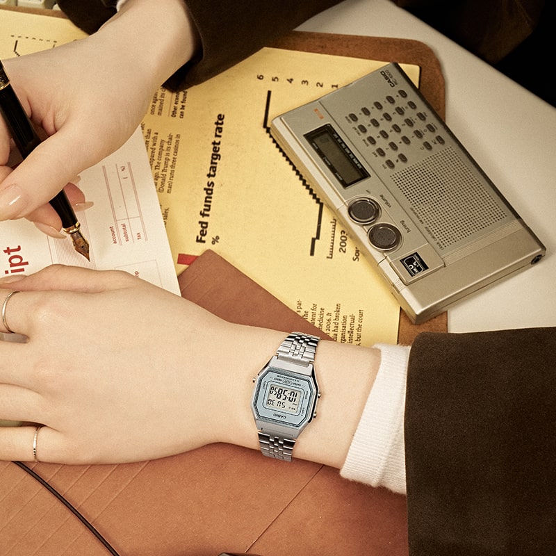 Close up image of a woman wearing a silver LA680 watch writing.