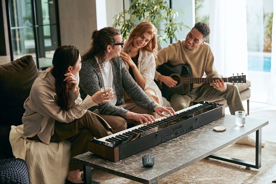 Group of musicians in on a couch surrounding a pianist playing PX-S6000 Group of musicians in on a couch surrounding a pianist playing PX-S6000