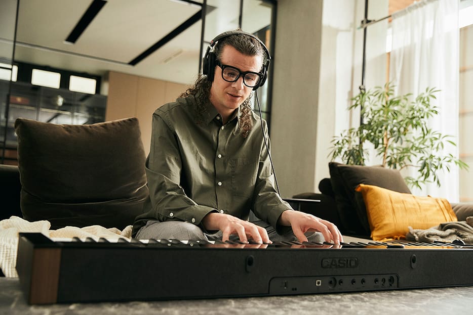 Front view of musician wearing headphones plugged into a PX-S6000 keyboard playing on a coffee table Front view of musician wearing headphones plugged into a PX-S6000 keyboard playing on a coffee table