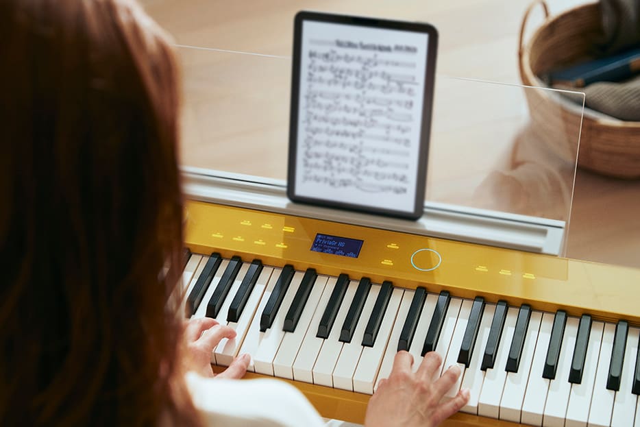 Yellow PX-S7000 keyboard being played with tablet displaying sheet music sits on clear music stand Yellow PX-S7000 keyboard being played with tablet displaying sheet music sits on clear music stand
