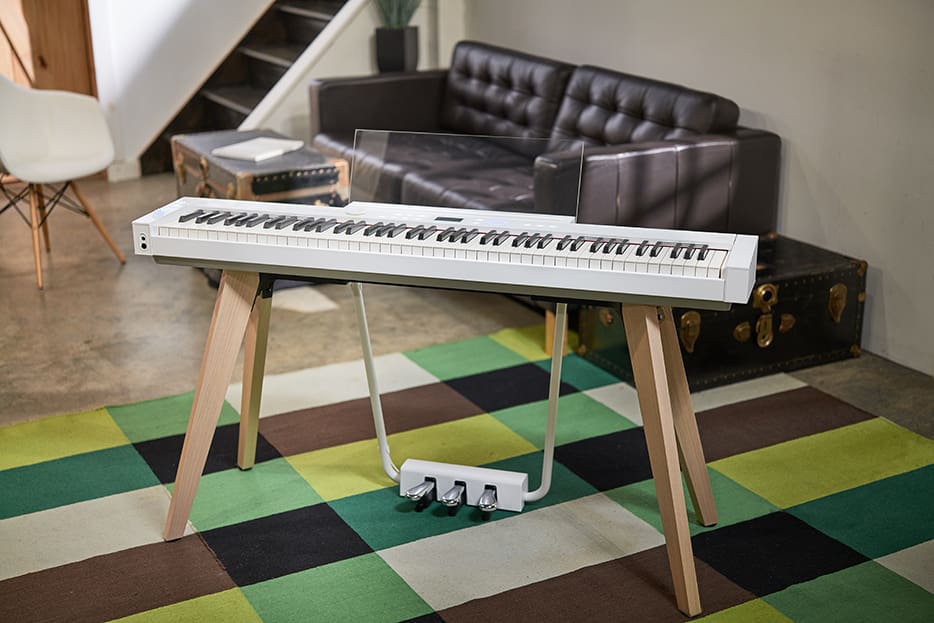 White PX-S7000 on stand on a green and brown rug in a room White PX-S7000 on stand on a green and brown rug in a room