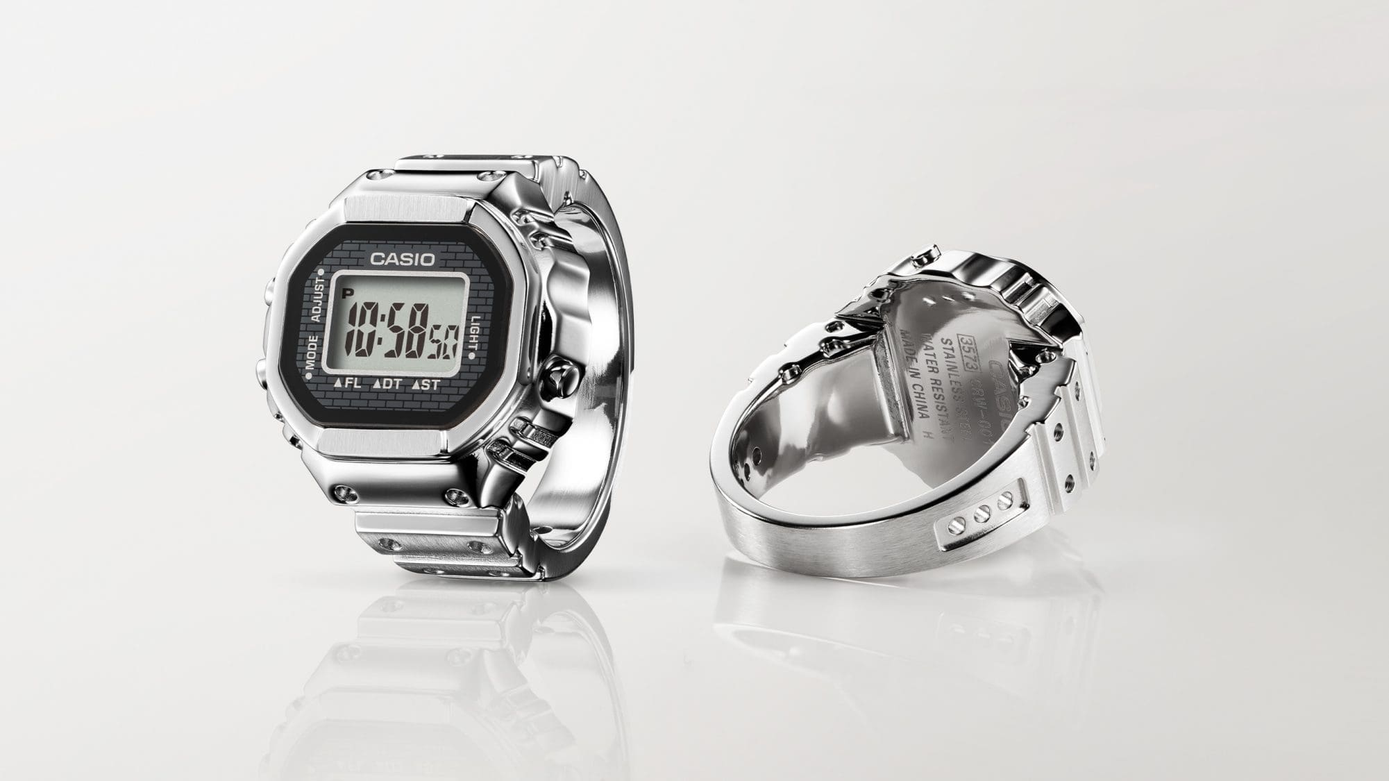 El reloj CASIO Ringwatch de pie y tumbado uno junto al otro para mostrar la pantalla digital y la parte trasera grabada.