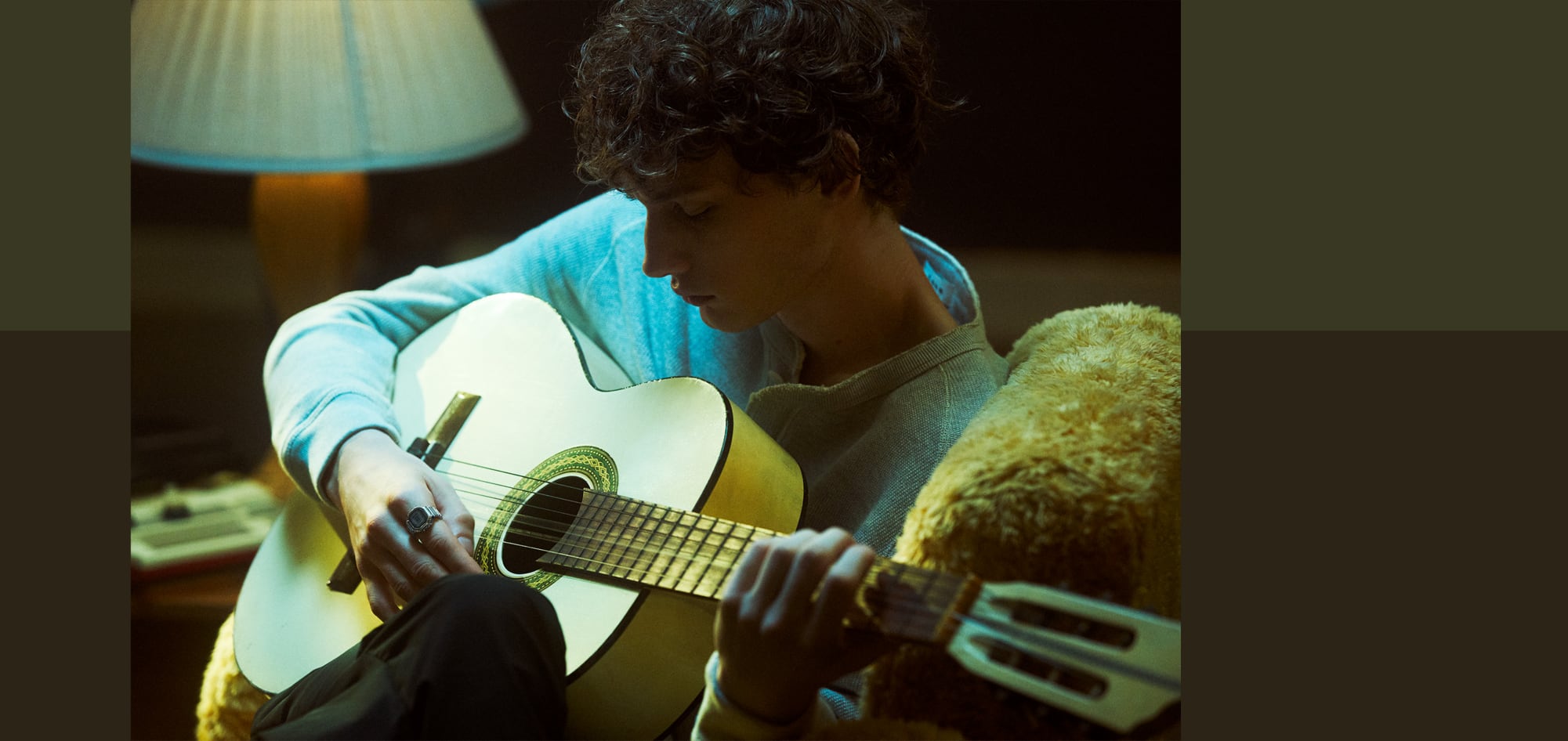 Imagen de medio cuerpo de un hombre tocando la guitarra en un sillón. Lleva el reloj CASIO Ring con anillo plateado y pantalla digital en el dedo índice.
