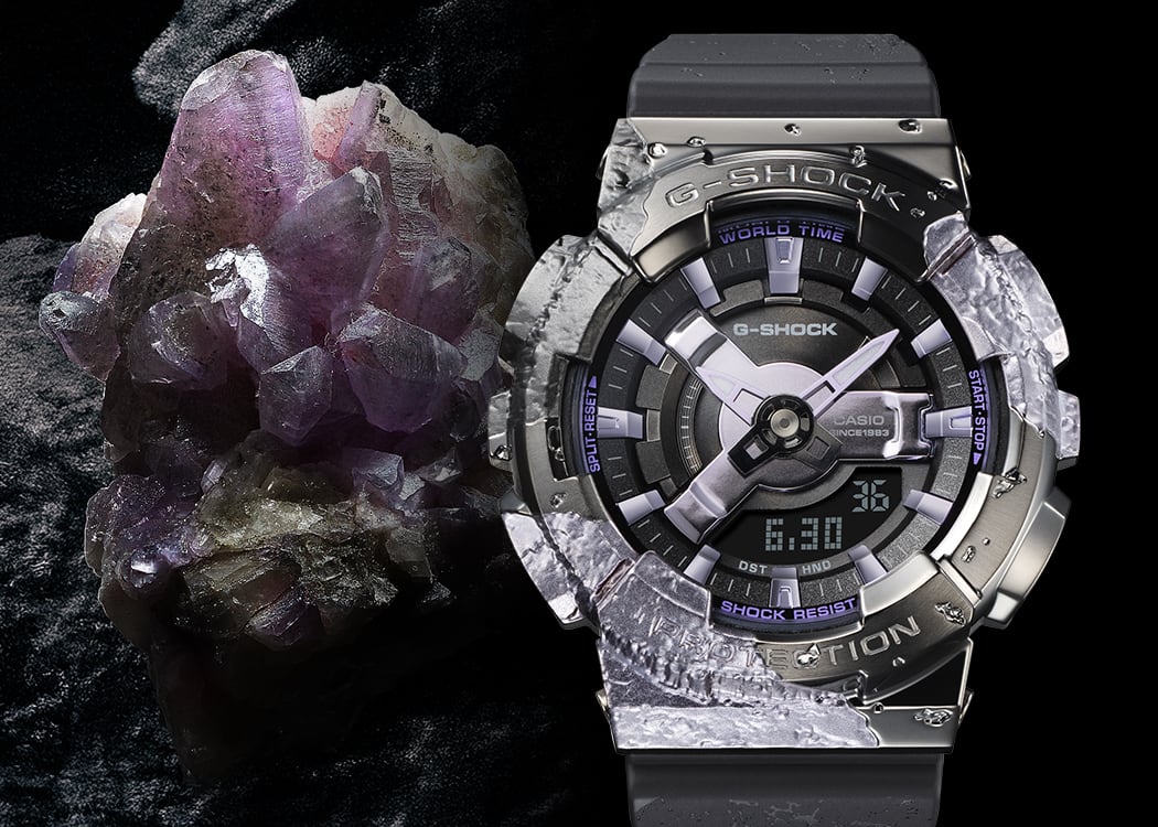 GM-S114GEM-1A2 El reloj aniversario GM-S114GEM-1A2, de color gris oscuro brillante, junto a un cristal de calcita de color púrpura brillante.