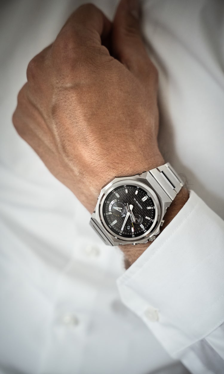 Primer plano de un hombre vestido con una camisa blanca y un reloj de pulsera GST-B1000 con esfera analógica negra.