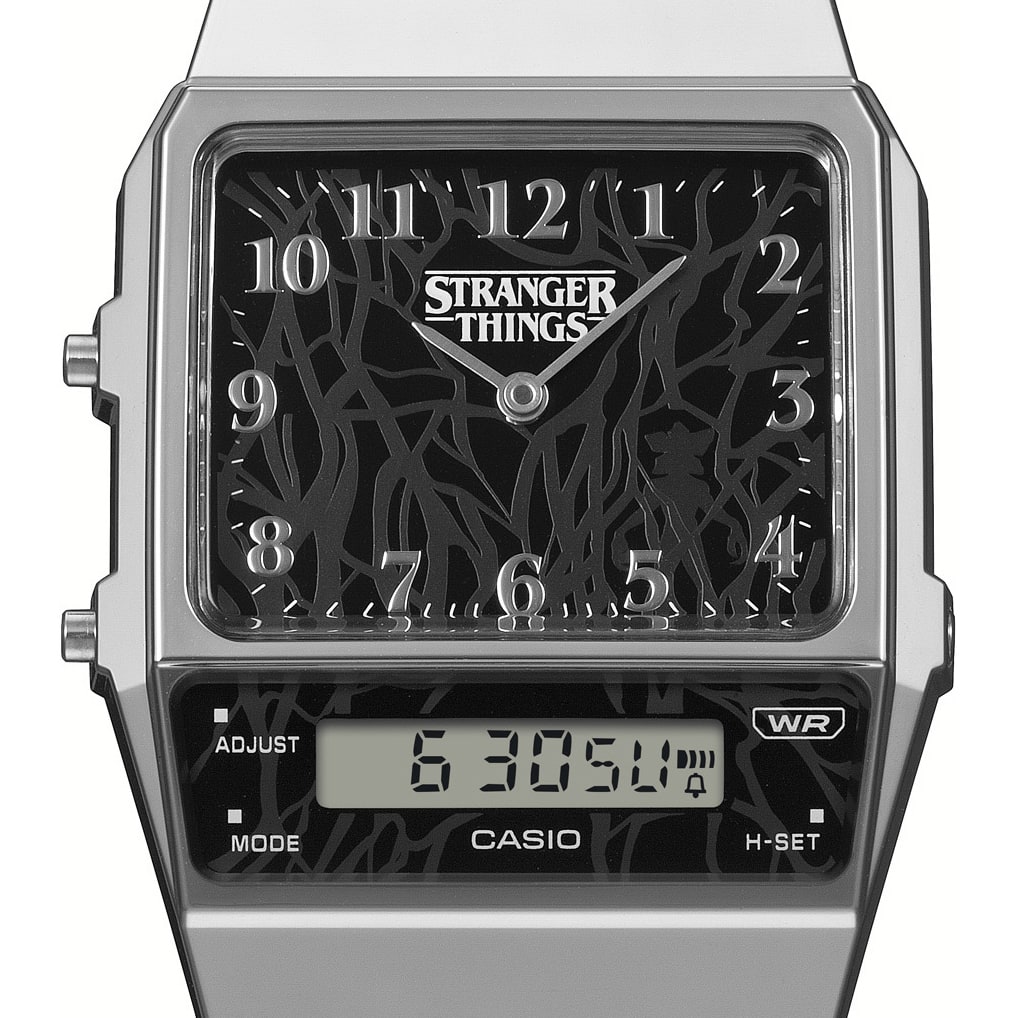 Primer plano del bisel rectangular negro del reloj analógico AQ-800EST-1A con el logotipo plateado y blanco de «Stranger Things» en la parte superior.