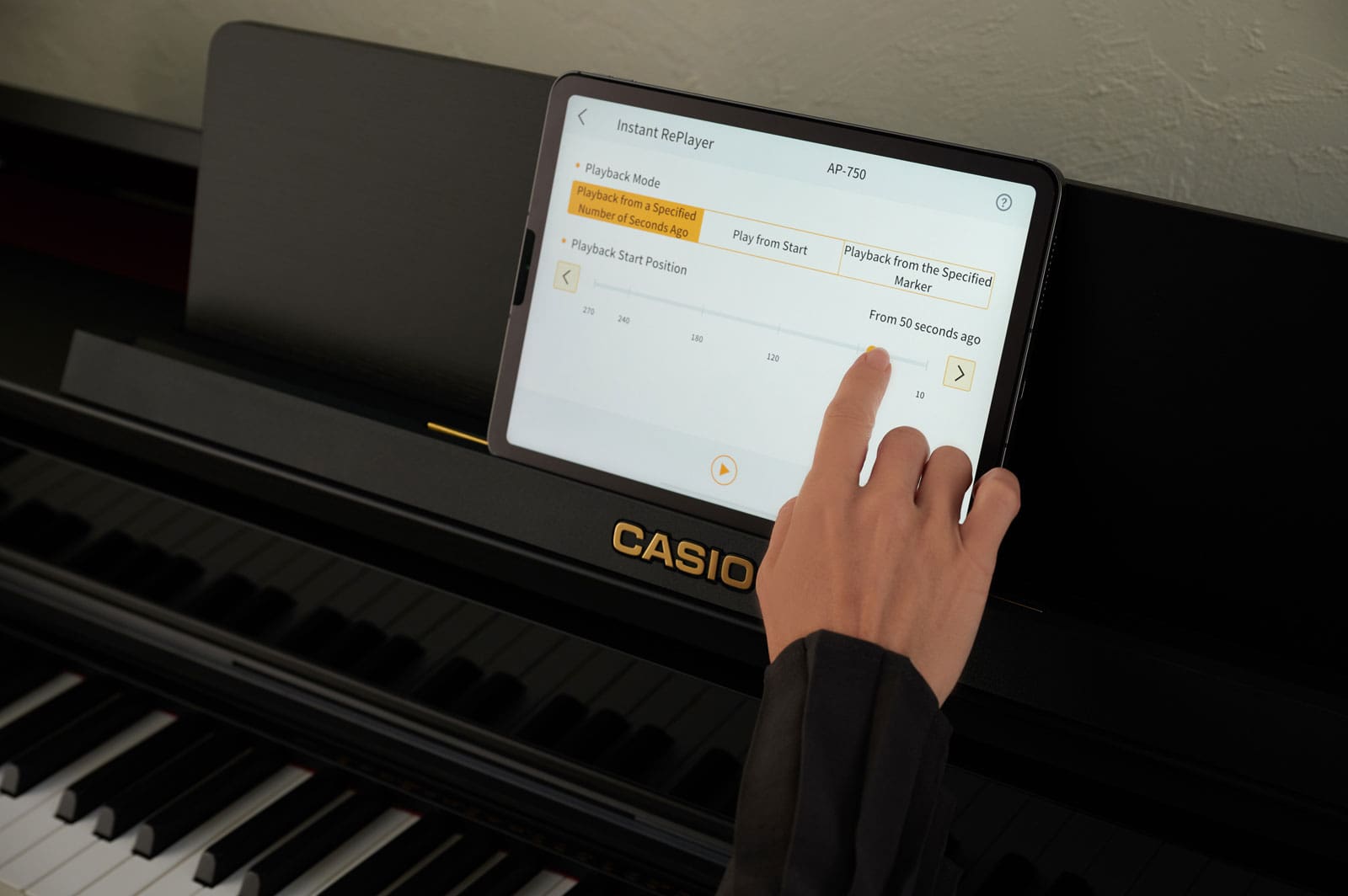 Una mano toca una tableta colocada en el soporte de partituras del piano digital AP-750 para manejar la aplicación «CASIO MUSIC SPACE»