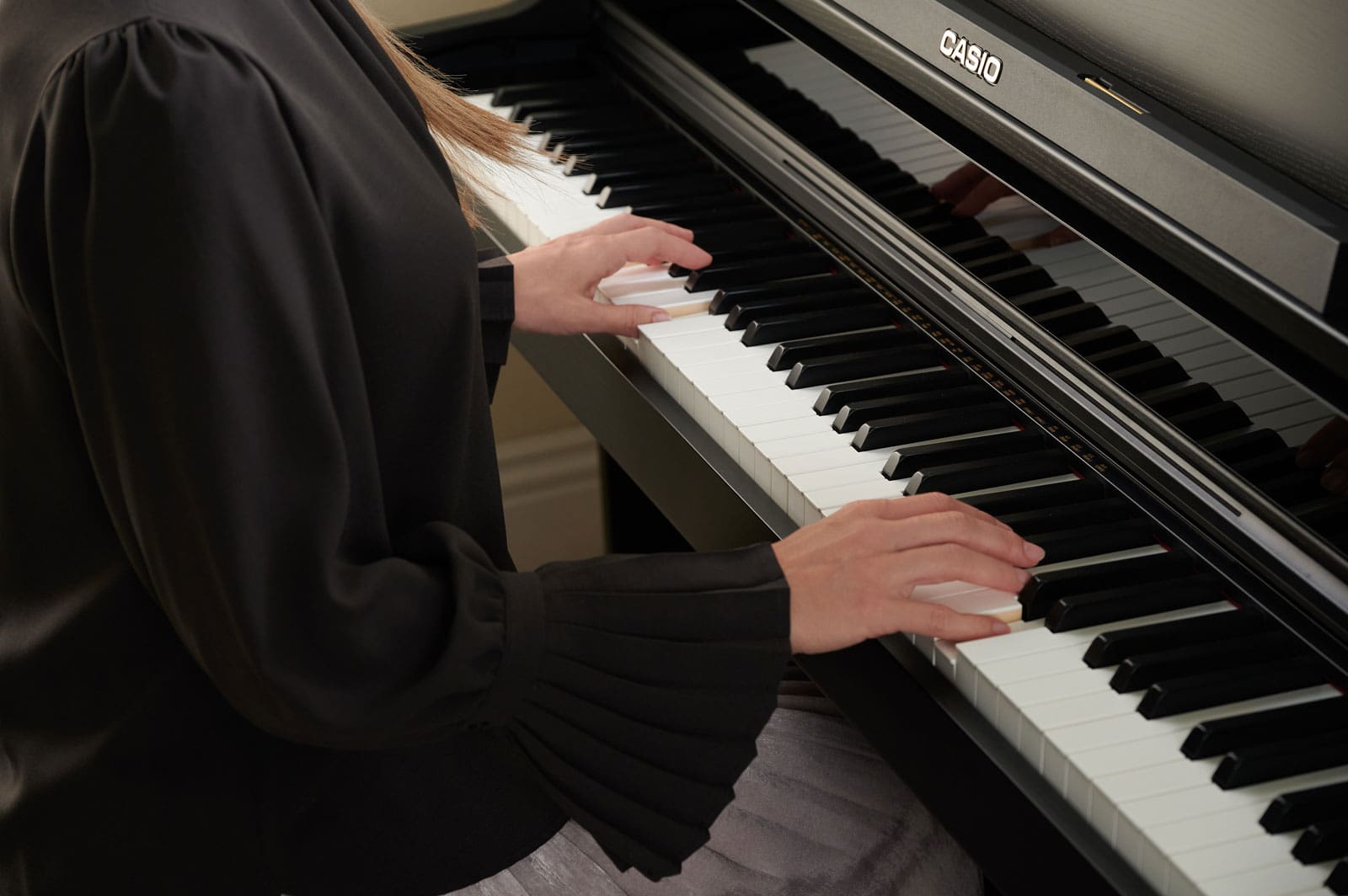 Una mujer elegantemente vestida está sentada al piano digital CASIO AP-750 tocando el piano