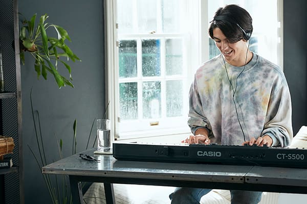 Un joven lleva auriculares y toca sonriente un Casiotone CT-S500