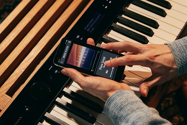 Alguien maneja el reproductor de música de su smartphone directamente sobre el teclado de un piano digital Privia PX-S3100