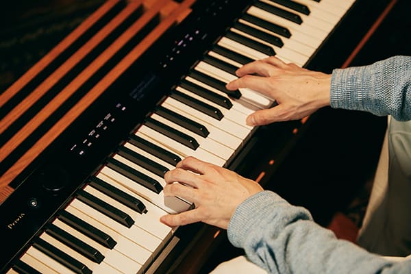 Primer plano del teclado del piano digital Privia PX-S3100BK negro y manos de hombre tocando el piano