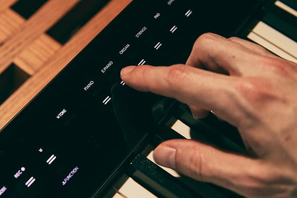 Primer plano de los controles táctiles del piano digital Privia PX-S3100BK negro, un dedo toca el campo táctil para el ajuste del piano eléctrico