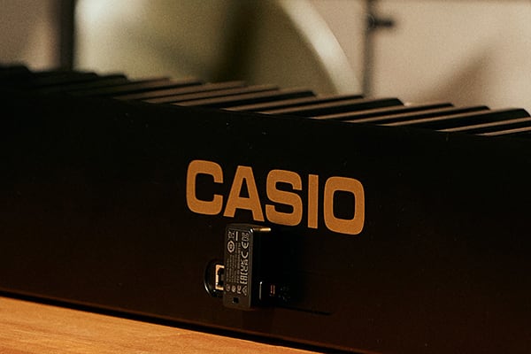 Primer plano de la parte posterior del piano digital CASIO PX-S5000 con adaptador MIDI y de audio