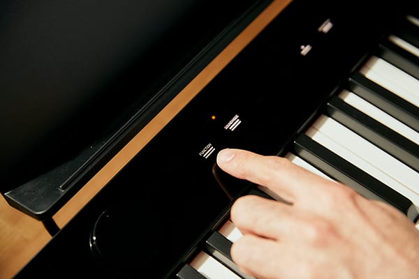 Primer plano de los controles táctiles del piano digital Privia PX-S5000 negro, un dedo toca un campo táctil