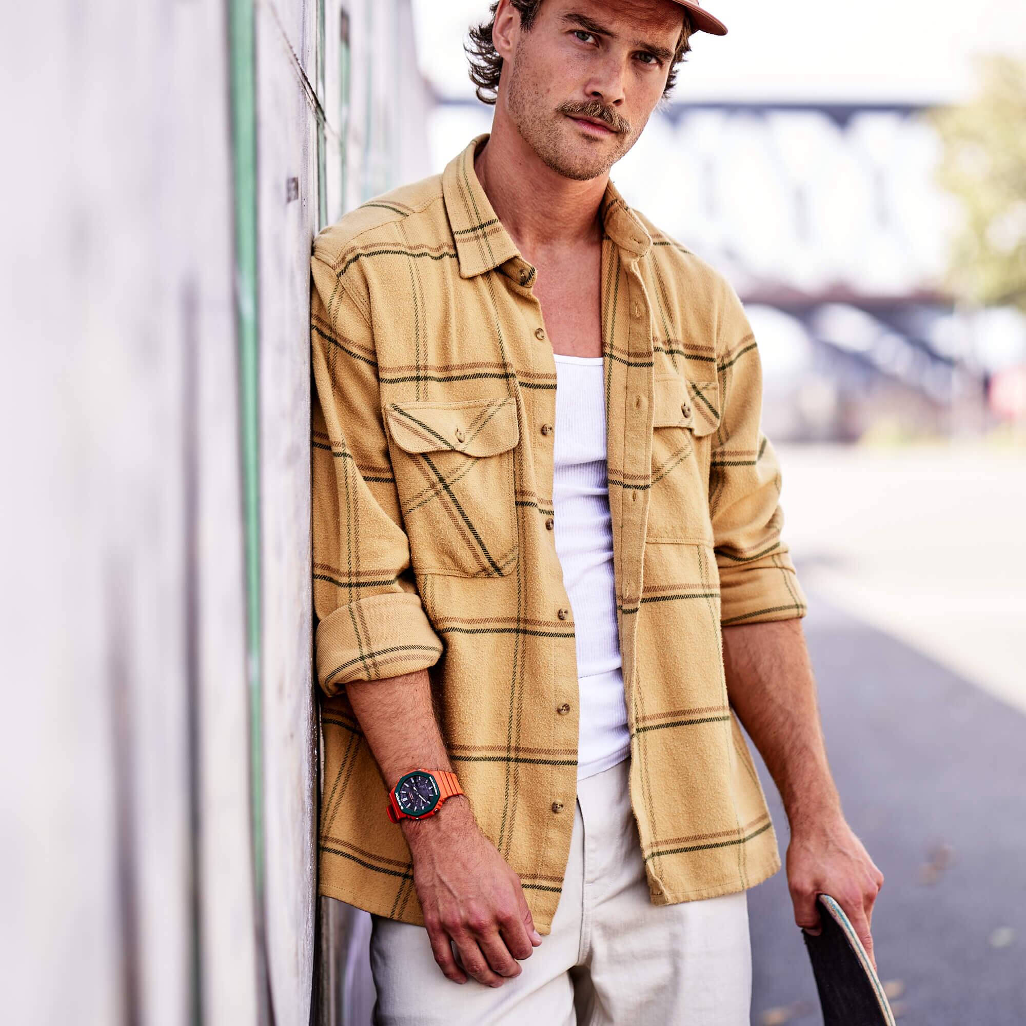 Un hombre con camisa de cuadros amarilla y gorra lleva el G-SHOCK 2110SC-4A.