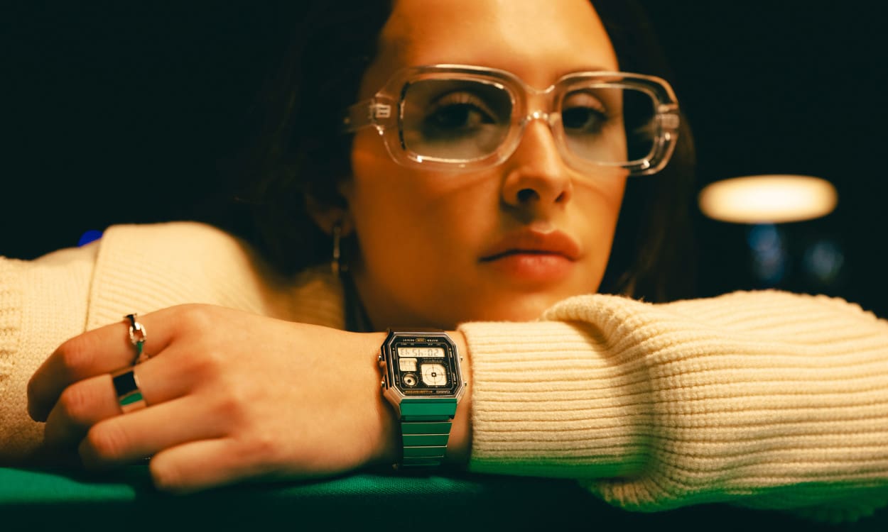 A130WE-1AEF Une femme s'appuie sur une table de billard, portant un pull blanc, des lunettes légèrement teintées et la montre-bracelet numérique A130WE-1AEF.