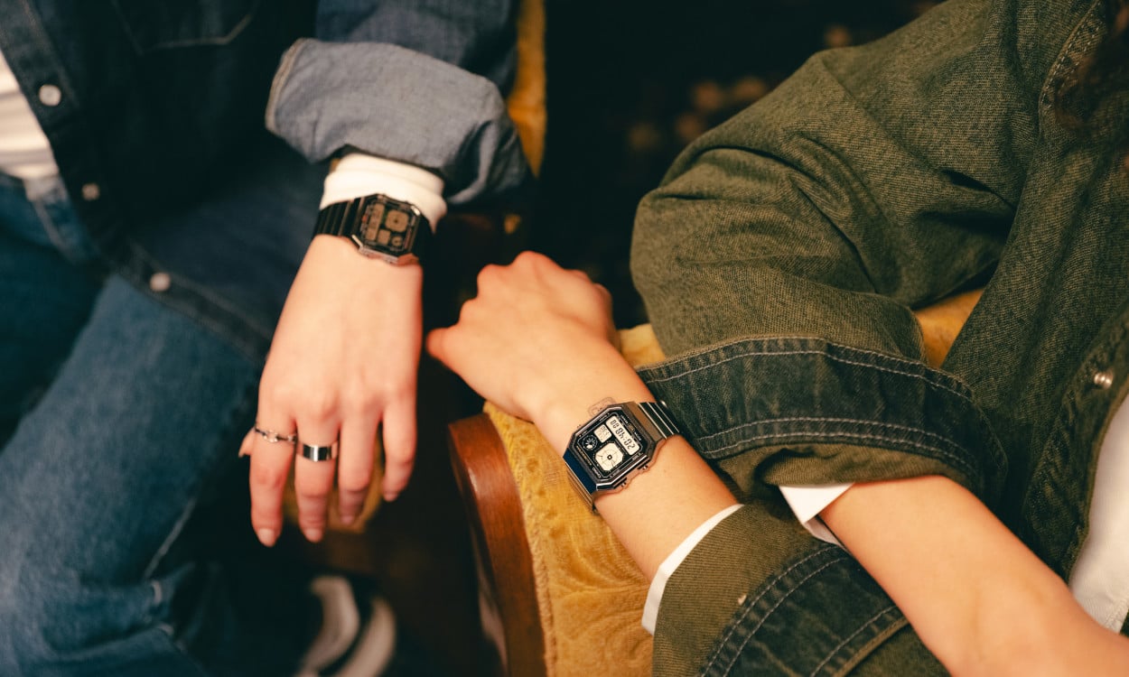 Deux personnes s'appuient sur un fauteuil, portant au poignet des montres-bracelets numériques 'A130' de la CASIO Vintage Collection.