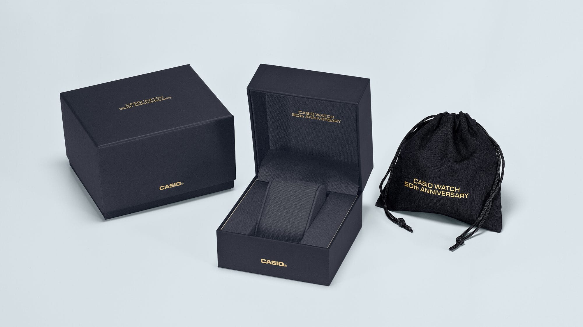 Boîte de montre Casio noire à côté d'un suremballage noir et d'un sac en tissu noir. Tous les éléments de l'emballage portent l'inscription dorée : Casio Watch 50th Anniversary.