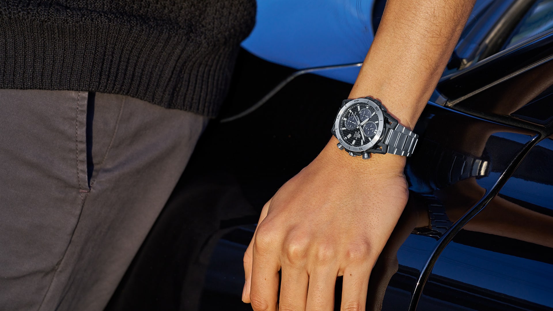 Une montre Casio Edifice EQS-960 avec un bracelet argenté au poignet d'une personne appuyée sur une voiture.
