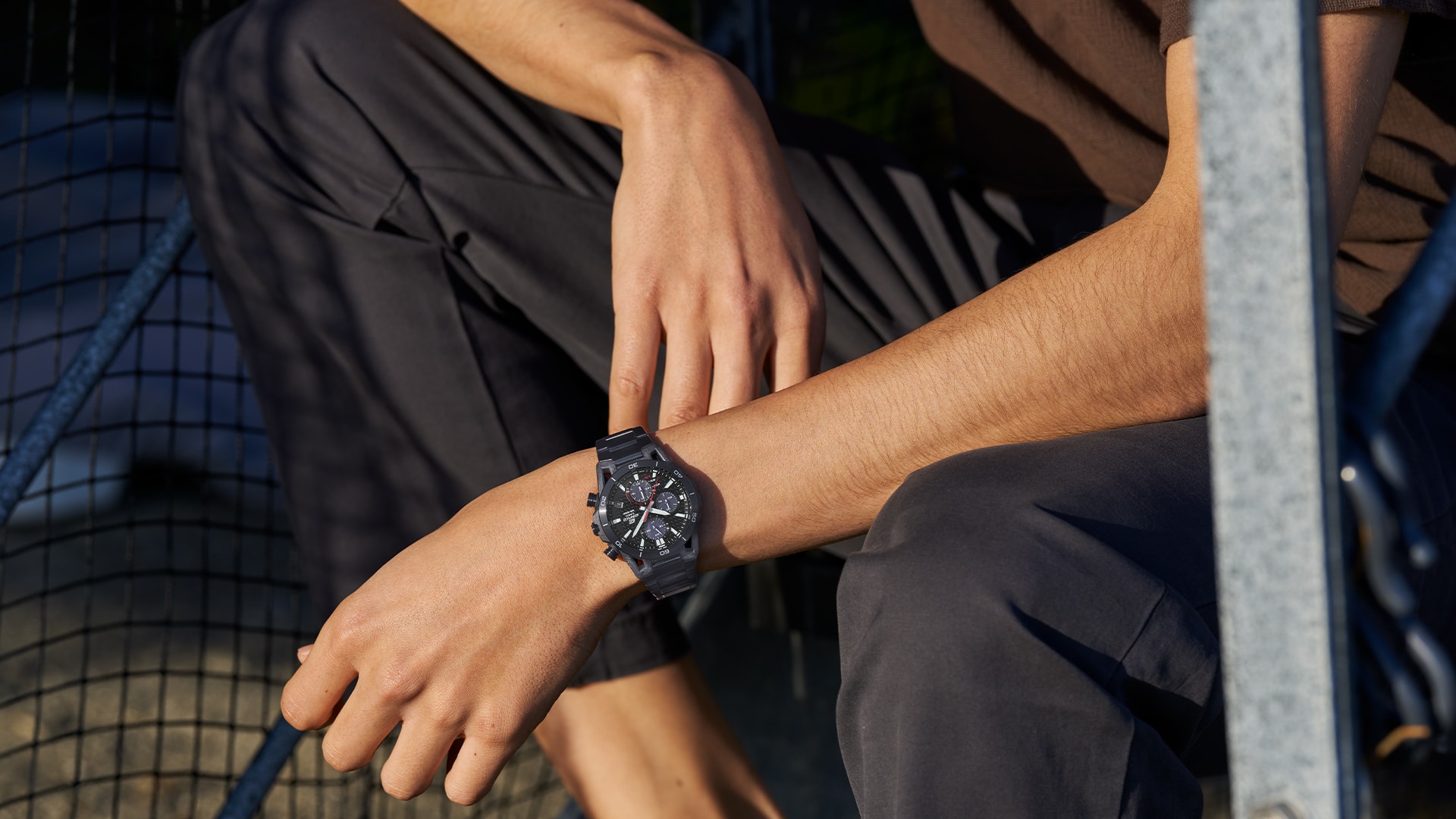 Une montre Casio Edifice EQS-960 avec un bracelet en plastique noir au poignet d'un homme accroupi devant un but de football.