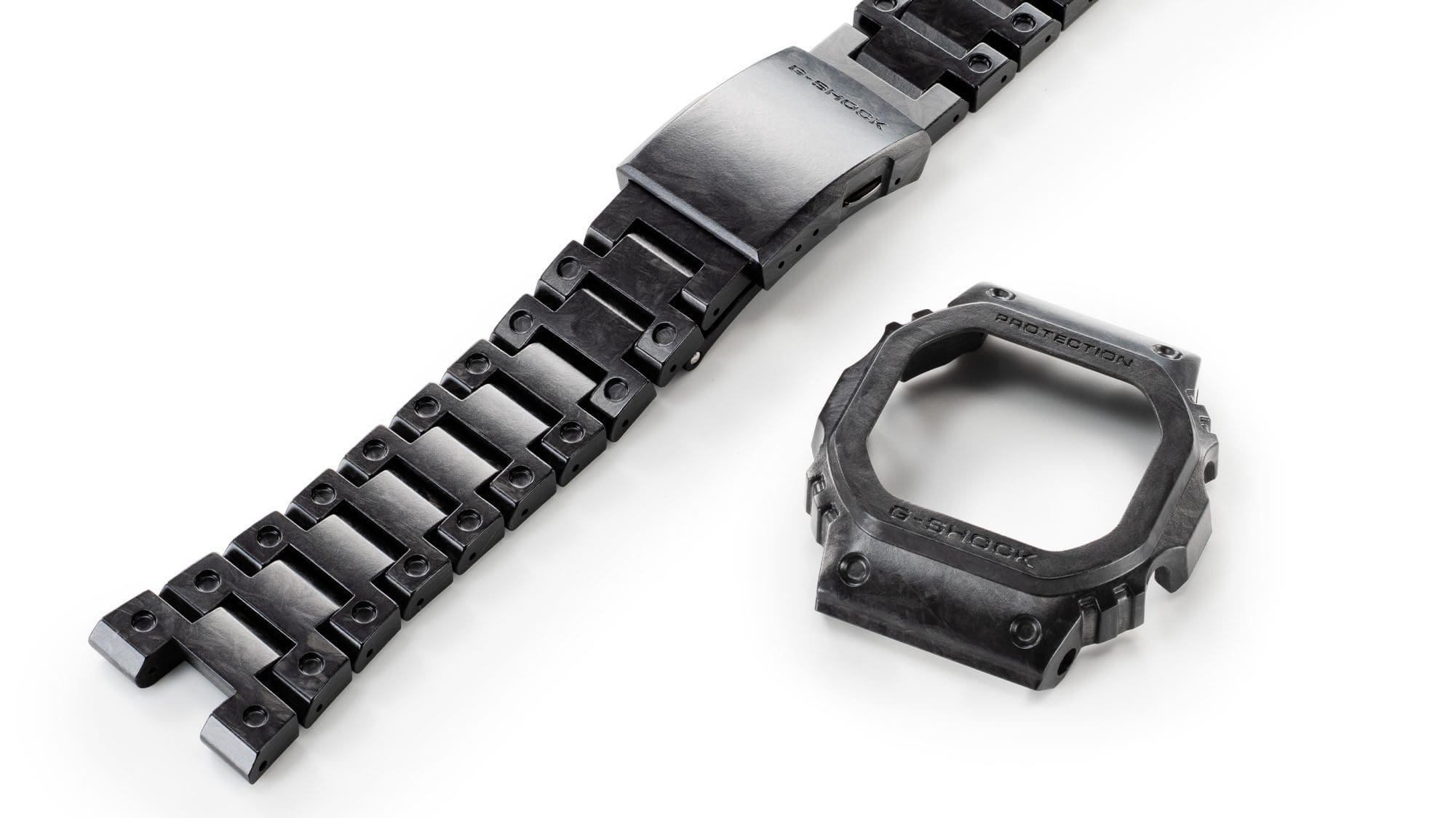 Le bracelet en carbone noir et gris de la Casio G-Shock GCW-B5000UN-1 avec fermeture One-Touch, à côté duquel se trouve le boîtier gris et noir.