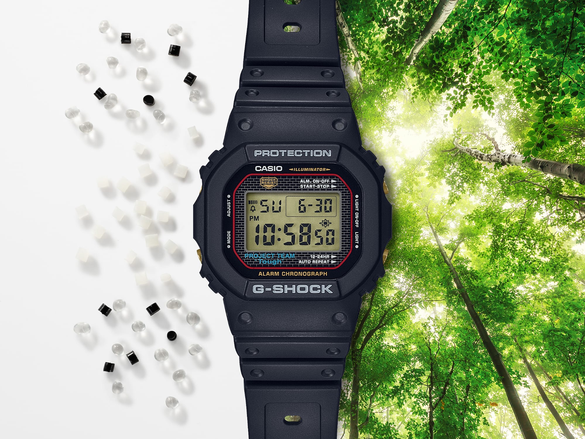 La Casio G-Shock DW-5040PG-1 noire entre des granulés de résine transparents, blancs et noirs sur fond blanc et un feuillage baigné de lumière