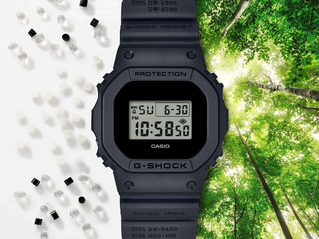 La Casio G-Shock DWE-5657RE-1 noire entre des granulés de résine transparents, blancs et noirs sur fond blanc et une canopée baignée de lumière