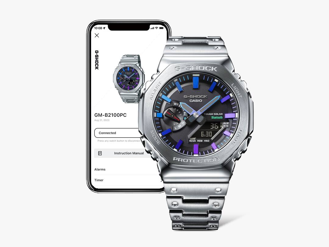 Une montre Casio G-Shock entièrement métallique avec un bracelet en acier inoxydable argenté et un cadran noir devant un smartphone dont l'écran affiche des informations sur la montre.
