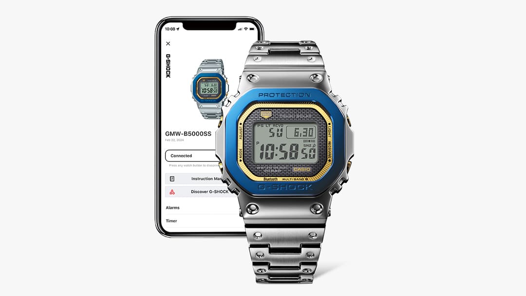 La montre-bracelet anniversaire Casio G-Shock GMW-B5000SS-2 avec bracelet en acier inoxydable argenté, lunette bleue et bord de cadran doré devant un smartphone sur l'écran duquel sont affichées des informations sur la montre.