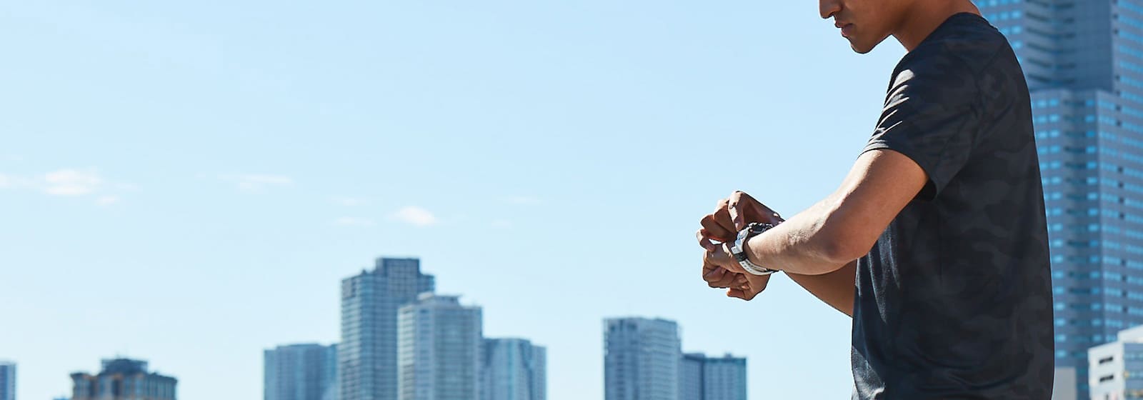Un homme se tient devant une ligne d'horizon de gratte-ciel et regarde sa montre de sport Casio G-Squad GBD-100-1A7