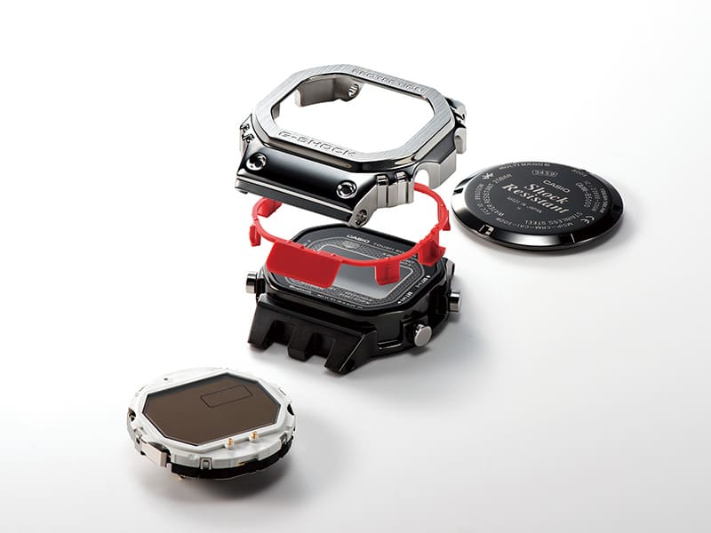 Boîtier, composant tampon rouge et lunette en titane argenté d'une montre GMW-B5000D-1 représentés séparément l'un au-dessus de l'autre, à côté se trouvent le dos du boîtier et l'écran.