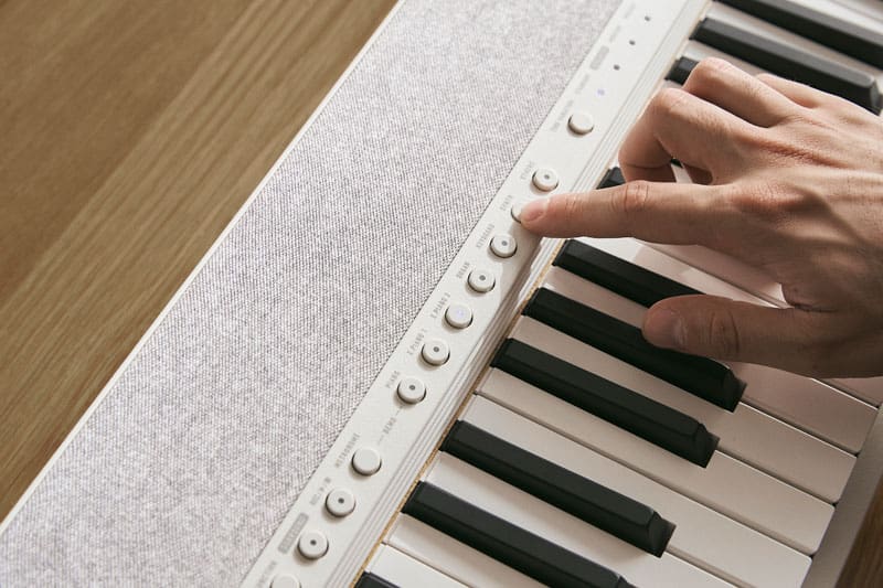 Gros plan sur le clavier et le panneau de commande du CT-S1-76WE blanc, un doigt appuie sur un bouton du panneau de commande.