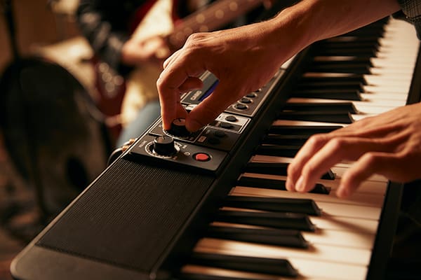 Gros plan sur le clavier d'un Casiotone CT-S500, une main touchant un bouton du panneau de commande, l'autre main jouant sur le clavier