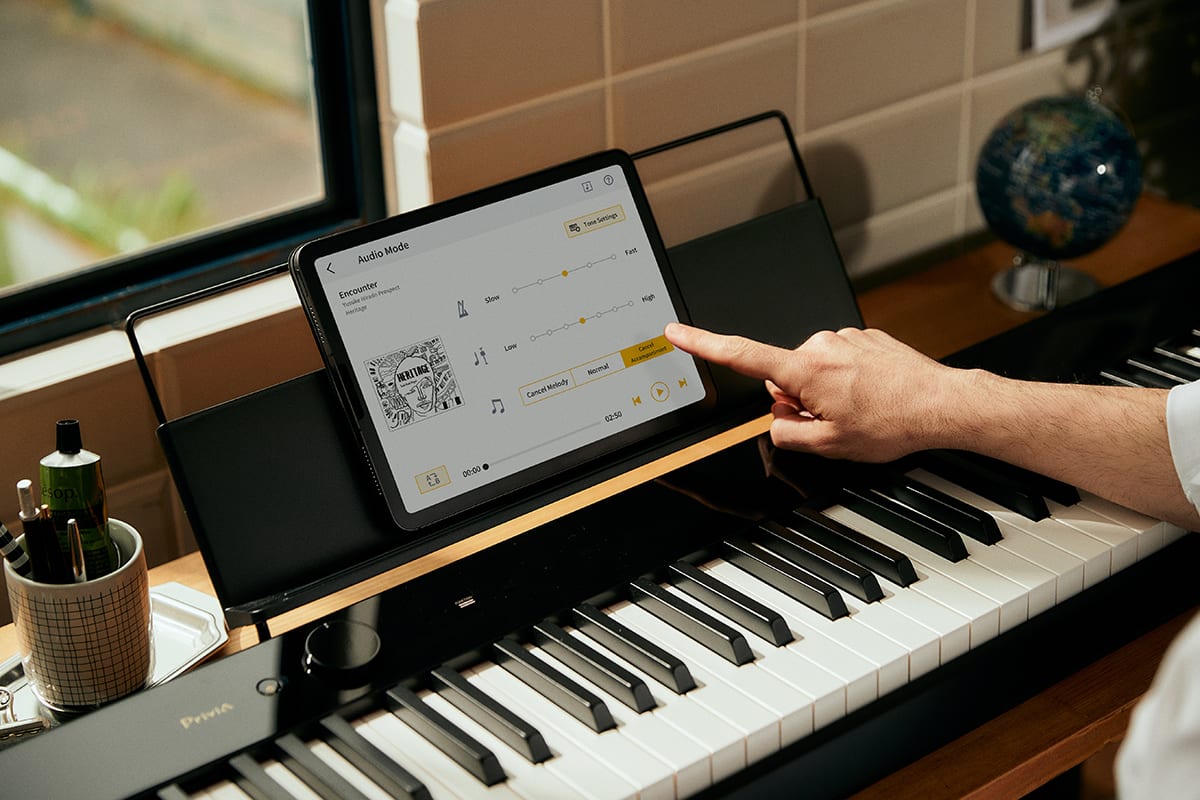 Une main touche une tablette posée sur le pupitre du piano numérique Privia PX-S5000.
