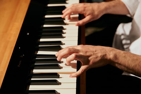 Gros plan sur le clavier du piano numérique noir Privia PX-S5000 et sur des mains d'homme jouant du piano.