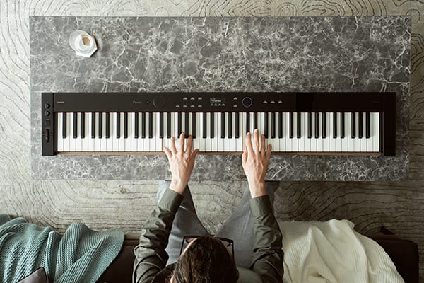 Vue d'en haut d'une personne assise sur un canapé et jouant sur un piano numérique posé sur la table du salon devant elle