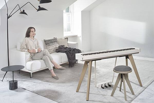 Une femme assise sur un canapé dans un salon lumineux regarde le piano numérique blanc PX-S7000WE