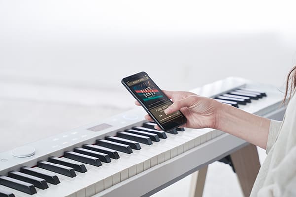 Quelqu'un utilise le lecteur de musique de son smartphone au-dessus du clavier d'un piano numérique PX-S7000WE